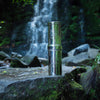 An American Reserves British Berkefeld 1 Liter Stainless Steel Gravity System & Ultra Sterasyl sits on a mossy rock, gleaming as ultra-pure water flows from the waterfall, surrounded by lush greenery.