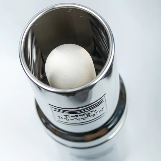 A silver metal container with an open top cradles a white, round American Reserves British Berkefeld 1 Liter Stainless Steel Gravity System & Ultra Sterasyl inside.