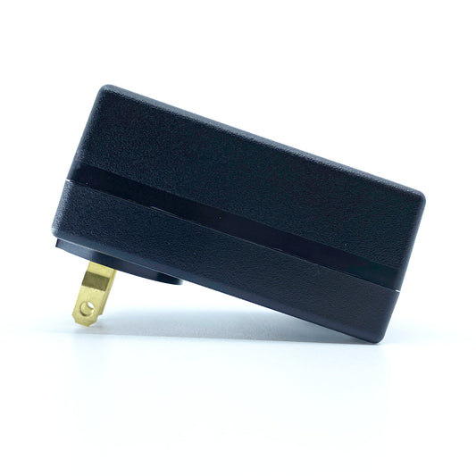 A black electrical charger with a two-prong plug from American Reserves lies flat on a white surface, appearing oddly serene despite its readiness for any DEFCONâ„¢ EMP Alert System activation.