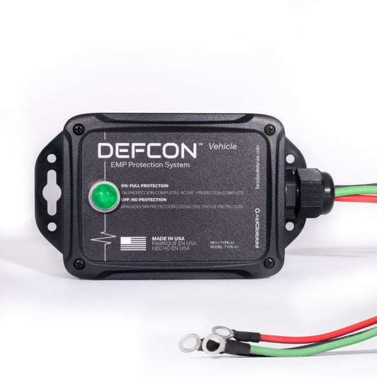 The DEFCONâ„¢ Vehicle + EMP Vehicle Protection Kit by American Reserves is a black rectangular system that protects against electromagnetic pulses, featuring a green indicator light with red and green wires.