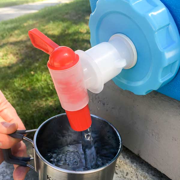 Water from the American Reserves AquaBrick 6 Pack Container flows into a metal mug held outdoors.