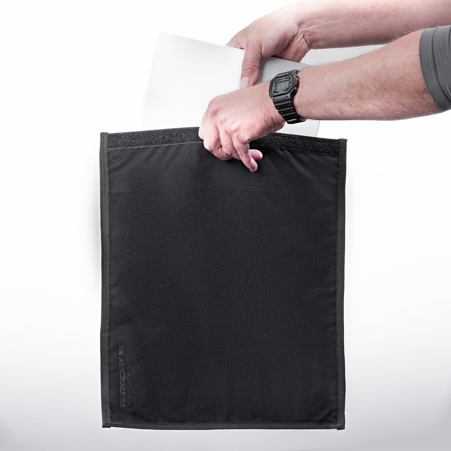 A person effortlessly slides their laptop into a sleek black protective sleeve, their watch glinting in the light. This American Reserves CORDURA® Berry Compliant Faraday Tablet Jacket ensures signal blocking for enhanced security.