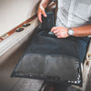 A person in a vehicle places an American Reserves CORDURA® Berry Compliant Faraday Tablet Jacket, featuring clear pockets for easy access, into the compartment near the cup holders. This sleek black organizer securely blocks signals as they navigate their journey.