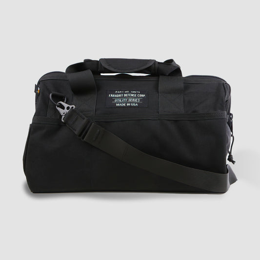 The black CORDURA® Utility Bag Medium by American Reserves, featuring a shoulder strap and a rectangular front label, serves as both a sleek duffel bag and a Faraday pouch for signal blocking. Its showcased on a plain gray background.