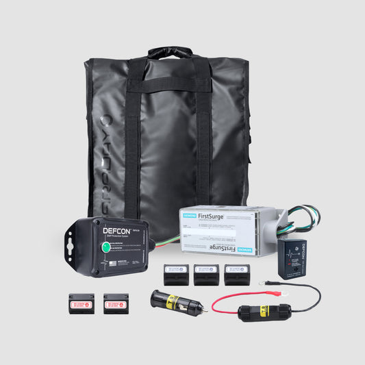 The Complete Auto And Home Protection EMP Kit by American Reserves, in sleek black, is designed to safeguard electronics like batteries, a power indicator, wires, switches, and a surge protector against EMPs. These components are meticulously arranged on a light gray background.