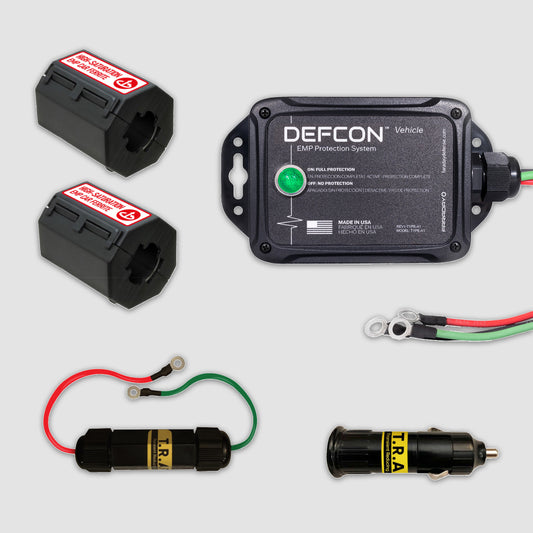 The DEFCONâ„¢ Vehicle + EMP Vehicle Protection Kit by American Reserves, featuring two black battery clamps, a DEFCON module, and cables with connectors for electromagnetic pulse protection, is displayed neatly on a light gray background.