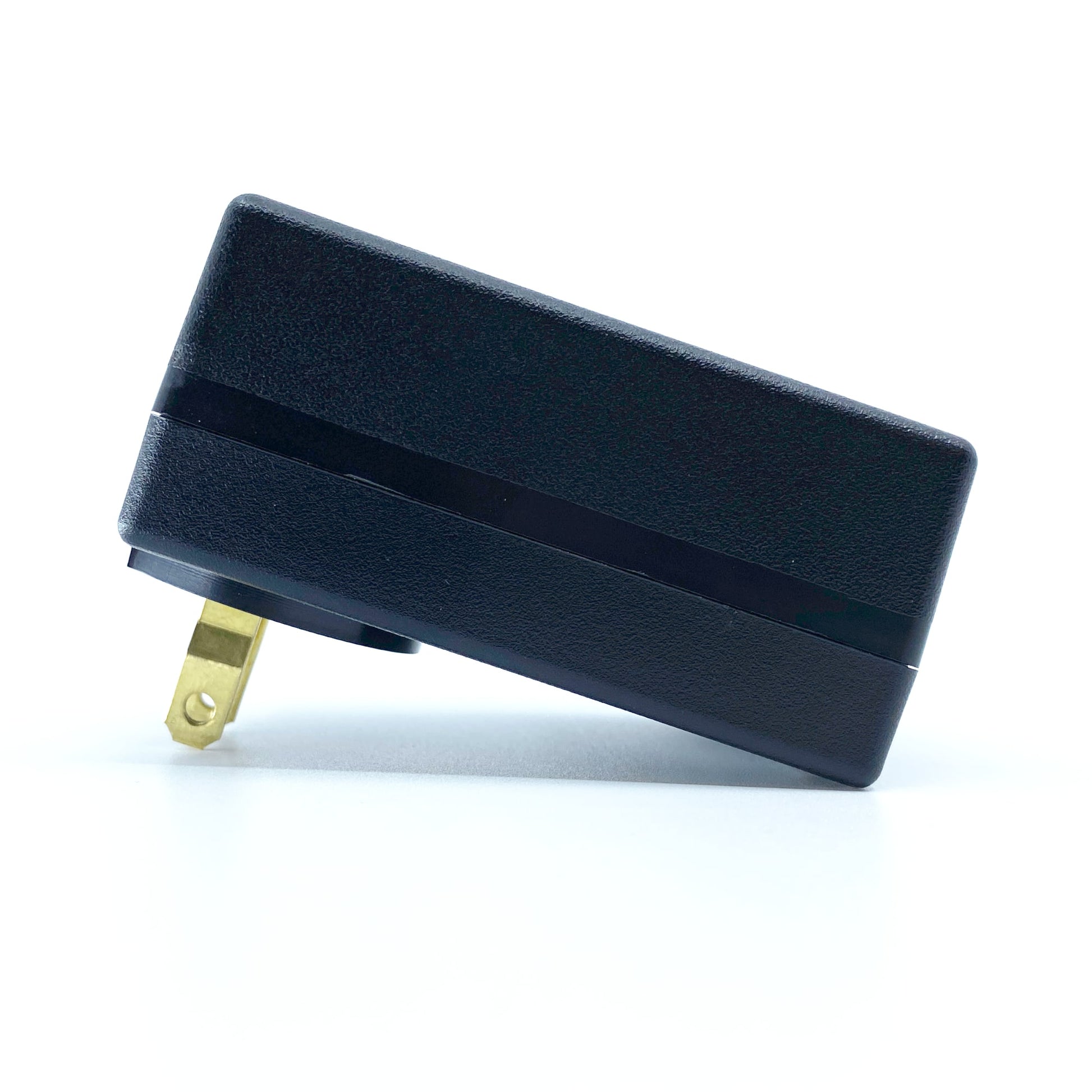 A black electrical charger with a two-prong plug from American Reserves lies flat on a white surface, appearing oddly serene despite its readiness for any DEFCON™ EMP Alert System activation.