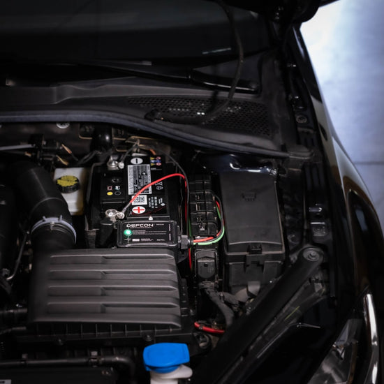 The car engine bay displays various components, including an American Reserves DEFCON™ Vehicle + EMP Vehicle Protection Kit, designed to shield against electromagnetic pulse damage.