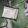 The American Reserves Anti-Hacking and EMF Shielding Bag lies on a cracked, green-painted ground with dry grass and a metal object nearby, crafted for superior protection.
