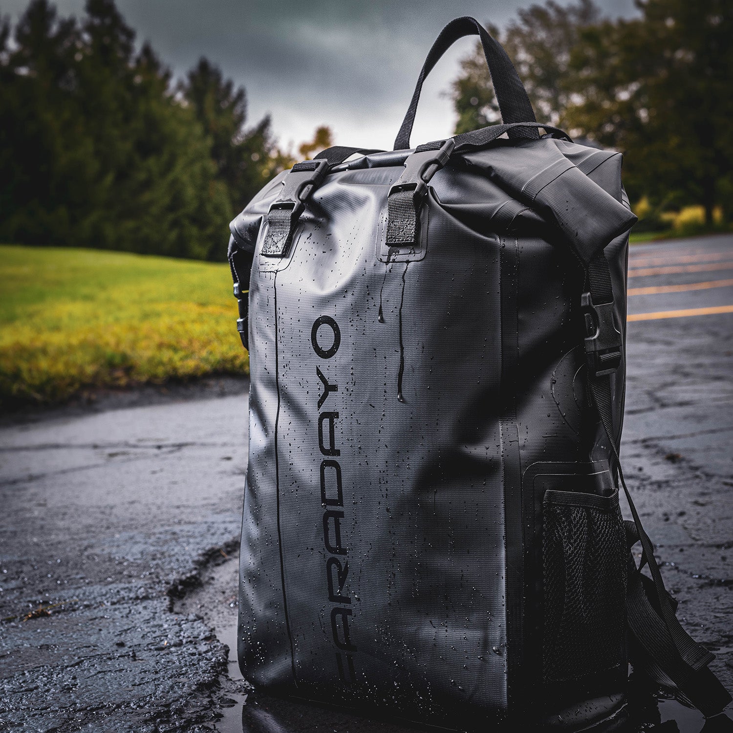 A Stealth Black Faraday Dry Bag Backpack from American Reserves, labeled FARADAY vertically, rests on a wet surface with trees in the background. It provides robust EMP protection to keep your devices secure while youre on the move.