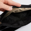 A hand unzips the sleek black Faraday Waist Pack from American Reserves, revealing a spacious interior with diamond-patterned lining. Its smooth texture offers RFID blocking for added security, featuring a visible zipper along the edge.