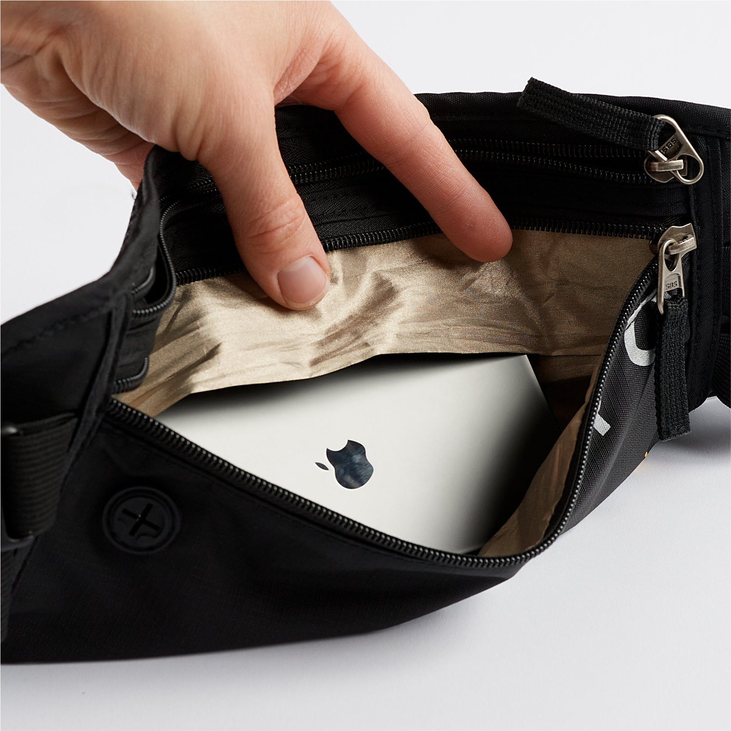 A hand holds open a sleek black zippered pouch, revealing a white Apple device inside. The American Reserves Faraday Waist Pack – RFID Belt Bag offers RFID blocking to shield your devices from scans and provides EMP protection for peace of mind.