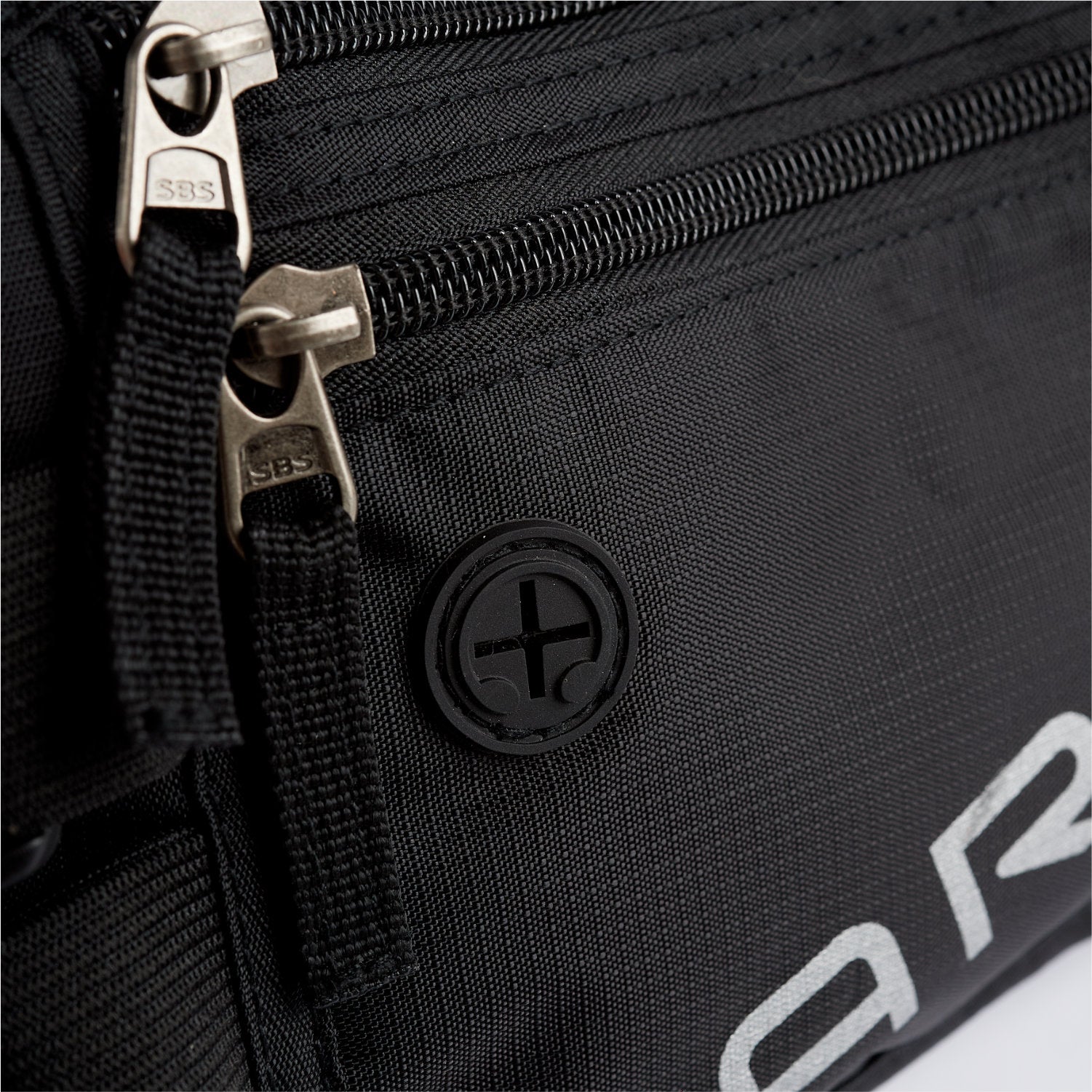 Close-up of American Reserves black Faraday Waist Pack featuring metal zippers, a plus-sign logo, part of a logo in white letters, and RFID blocking for added security.