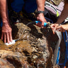 While camping, two people use their American Reserves RapidFlo Portable Water Filter to effortlessly purify water from a natural source and fill a container.