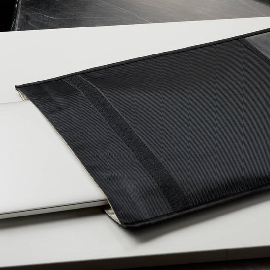 An American Reserves XXL Forensic Faraday Jacket Kit, serving as a Signal Blocking cover, partially encases a laptop on a white surface.