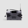 The American Reserves KA900 Voyager Max is a sleek, black receiver with a rectangular shape, digital display, buttons, and a smooth hand crank. Its telescopic antenna extends upward for emergency preparedness, ensuring connectivity.