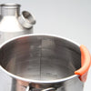 A Kelly Kettle® Ultimate Trekker Camping Kit by American Reserves, featuring a stainless steel camping kettle with an orange handle marked in milliliters and ounces, is prominently shown. A similar kettle in the background makes for perfect companions on your next outdoor adventure.