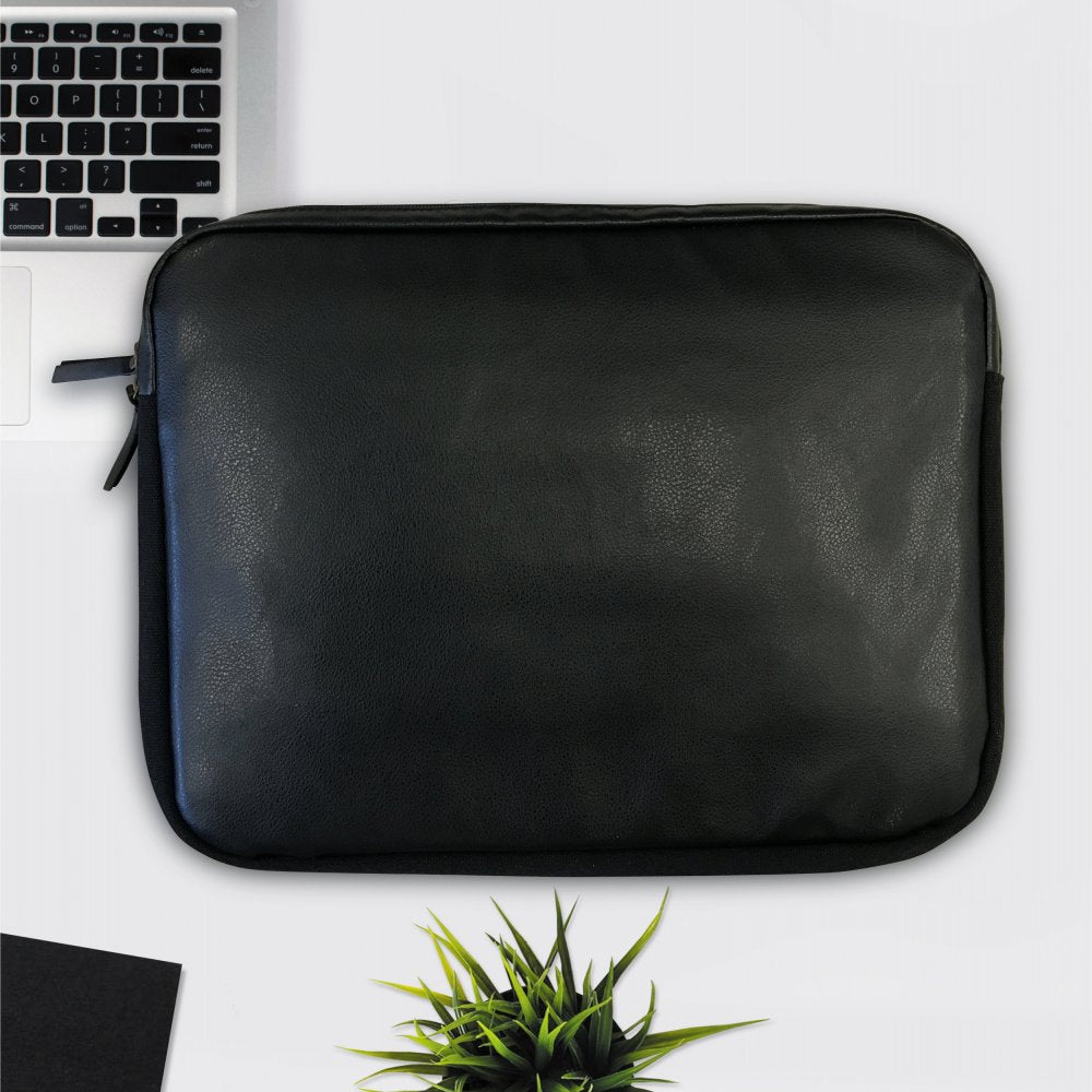 The PU Leather Large Privacy Protection Laptop Sleeve (9 x 13.5) by American Reserves lies on a white surface next to a partially visible laptop, small plant, and paper.