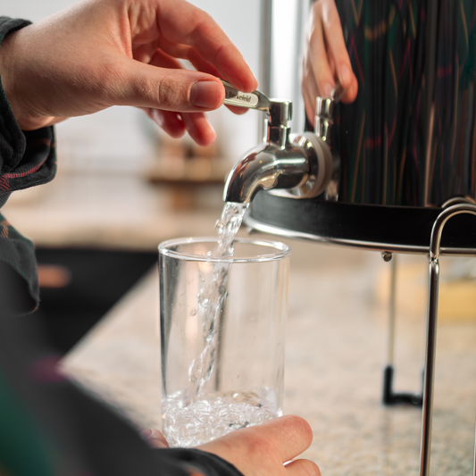 A person fills a clear glass with water flowing smoothly from the American Reserves British Berkefeld® Stainless Steel Gravity Tap.