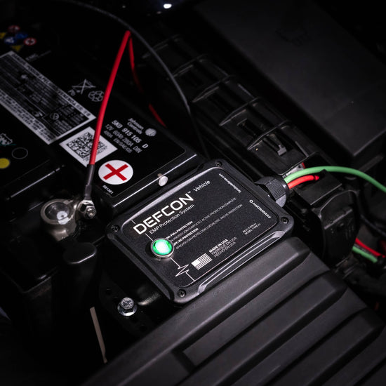 A close-up of an American Reserves Complete Auto And Home Protection EMP Kit connected to a car battery, featuring visible wires and a glowing green indicator. Ideal for auto and home defense, this device provides strong EMP protection.