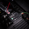 A close-up of an American Reserves Complete Auto And Home Protection EMP Kit connected to a car battery, featuring visible wires and a glowing green indicator. Ideal for auto and home defense, this device provides strong EMP protection.