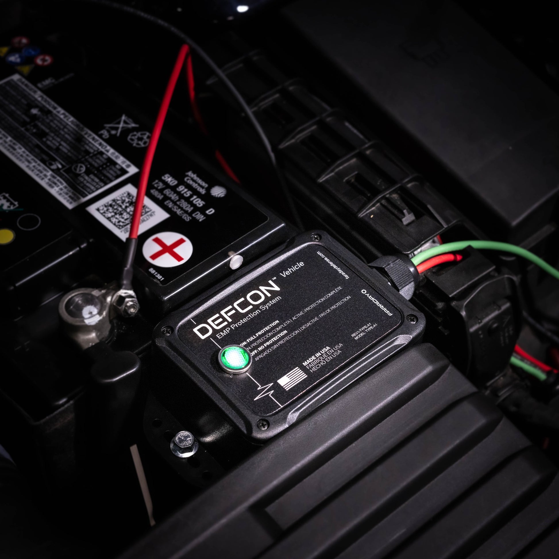 A close-up of an American Reserves Complete Auto And Home Protection EMP Kit connected to a car battery, featuring visible wires and a glowing green indicator. Ideal for auto and home defense, this device provides strong EMP protection.