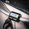 A high-saturation snap ferrite, part of the Complete Auto And Home Protection EMP Kit by American Reserves, is clamped onto a cable. In the background, theres a black panel and a twisted blue-white wire.