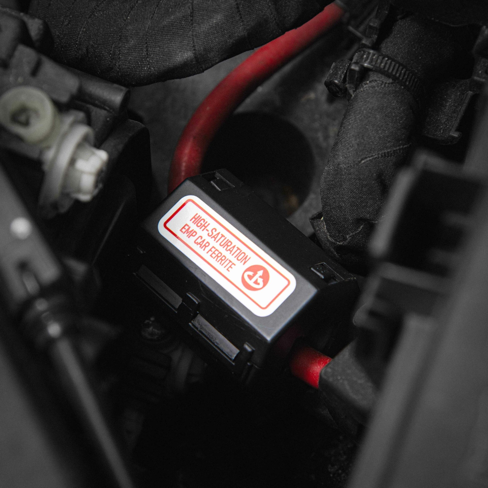 A close-up of a black electrical component with a High Saturation warning in English and French, surrounded by red and black wires. This setup is part of American Reserves Complete Auto And Home Protection EMP Kit, designed to guard against unexpected electromagnetic disturbances.